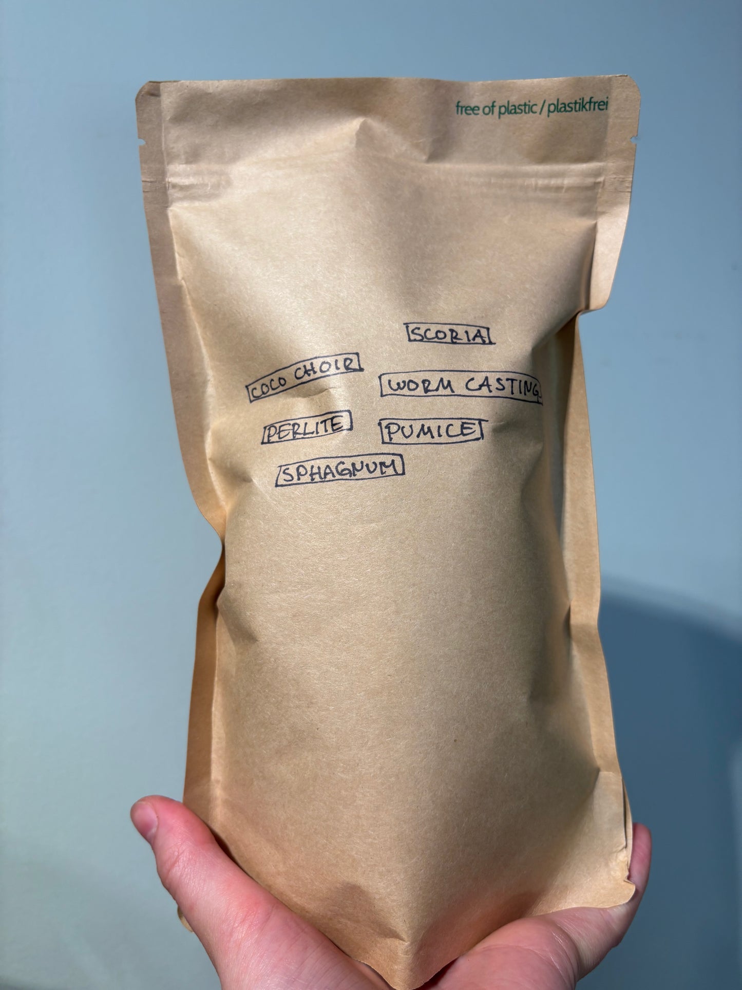 Hand holding labeled kraft paper bag of Home made Aroid Soil Mix listing ingredients like coco coir, perlite, pumice, and worm castings.